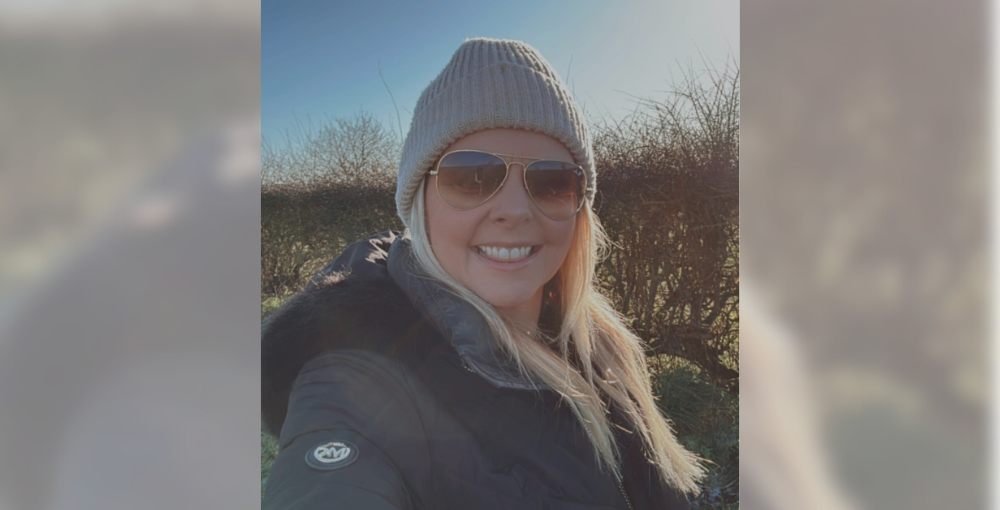 Blonde woman smiling in sunglasses and beanie hat.