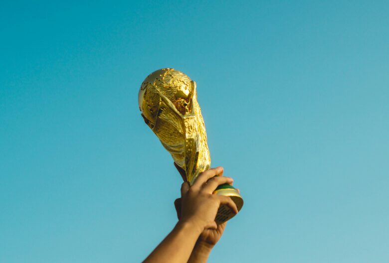 Hands holding up the FIFA World Cup Trophy against a bright blue sky, symbolizing victory and celebration.